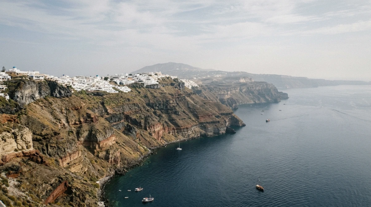 Catamaran anchored in a wide caldera panorama below the cliffs of Santorini during a Santorini boat tour, Greece
