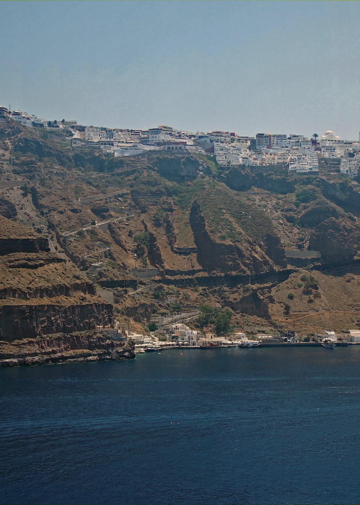The cliff-top town of Fira and the cable car track above the old port after a Santorini Oia sunset boat tour, Greece