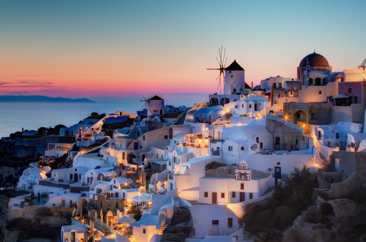 The windmills and whitewashed houses of Oia at dusk seen from the water after a Santorini sunset boat tour, Greece