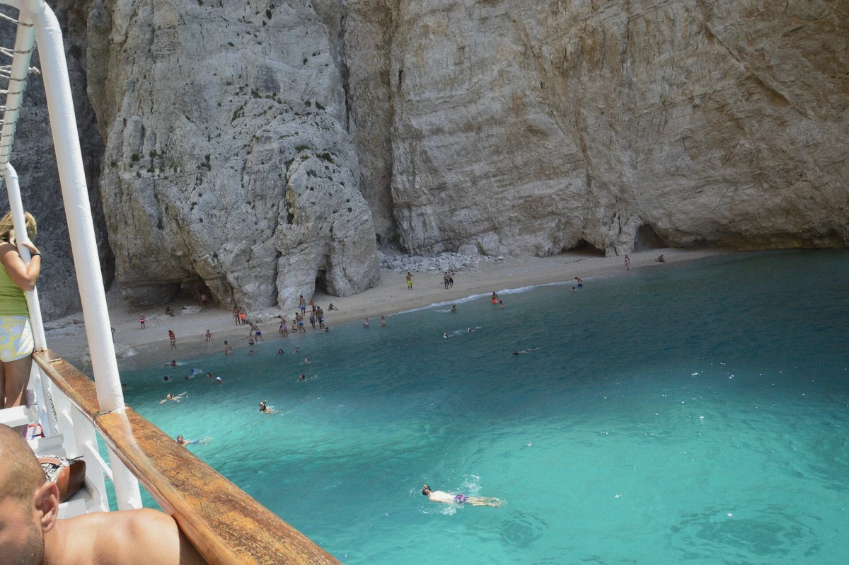 Swimmers in clear water beside a small boat under white cliffs on a self-driven Santorini boat day, Greece