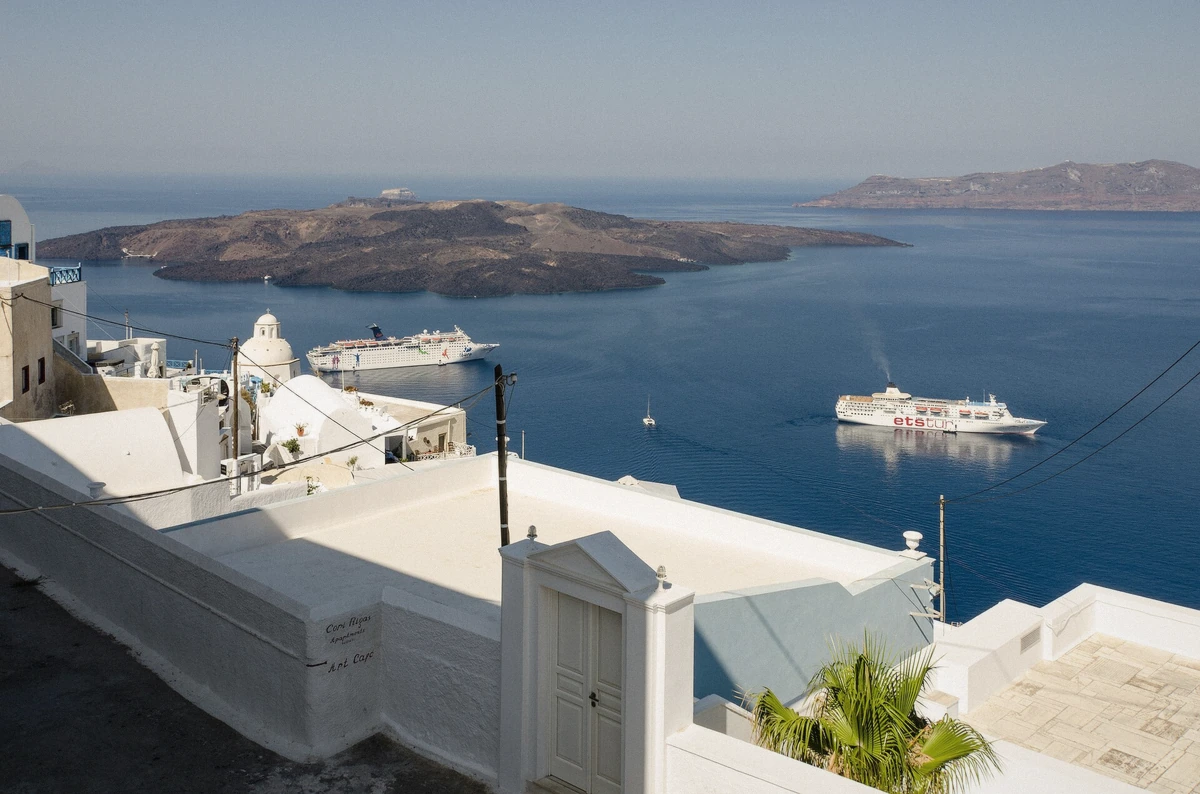 Tour boats crossing the caldera towards the dark lava dome of Nea Kameni during a Santorini boat tour, Greece