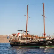 Traditional wooden boat anchored by the orange volcanic rocks of Nea Kameni during a Santorini boat tour, Greece